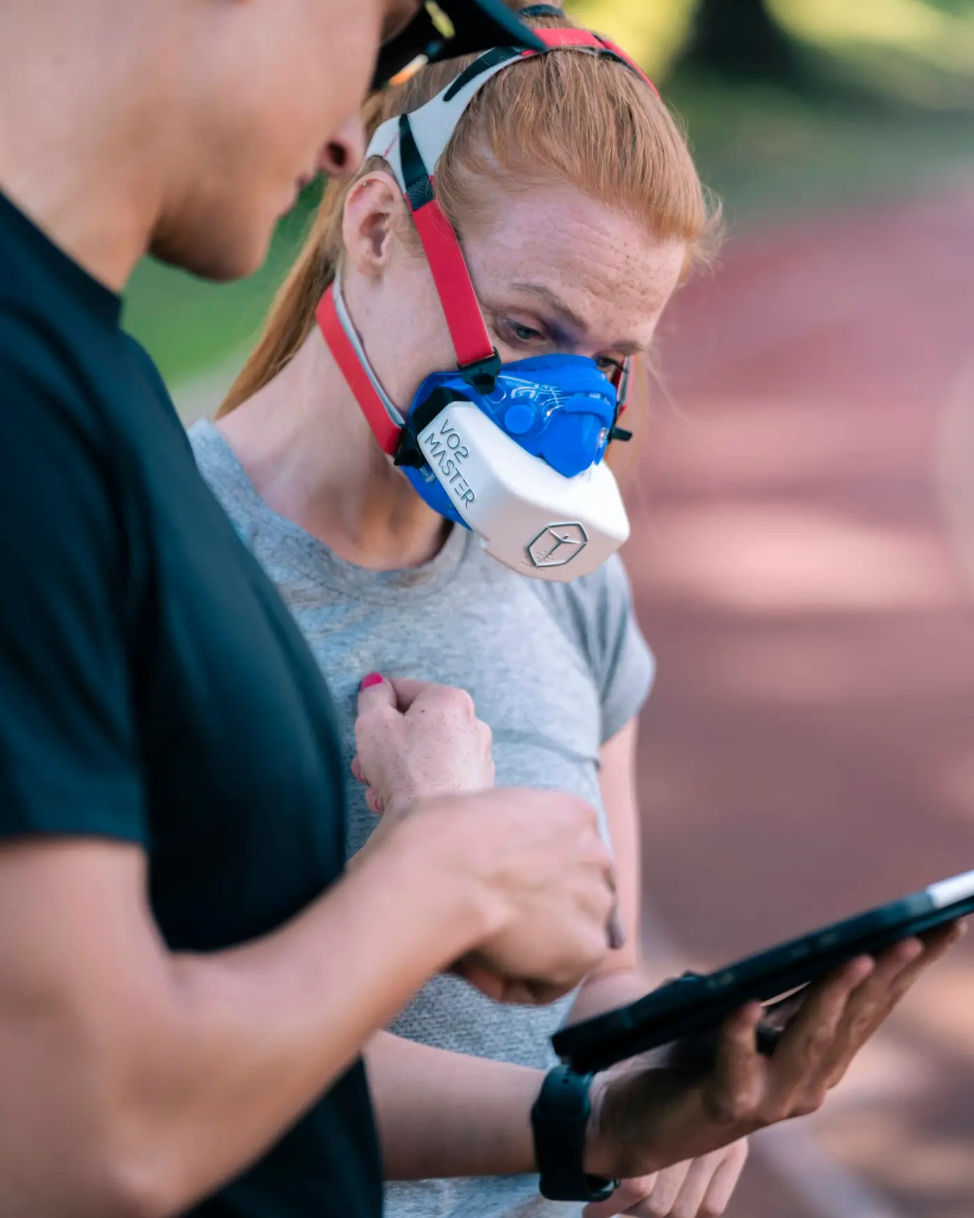 Coach mit Tablet an der Bahn, Athletin mit Atemgasmaske