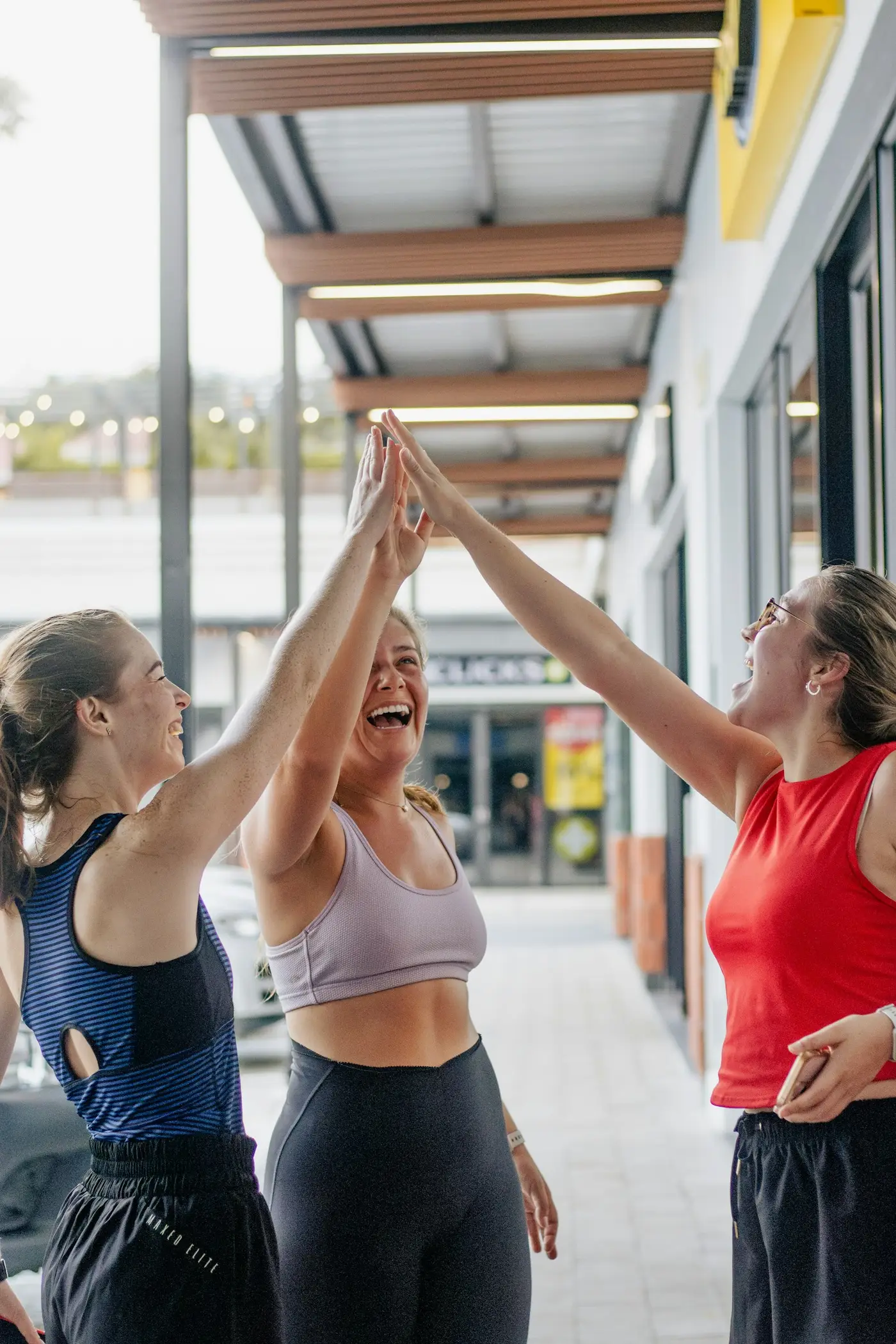 Drei Frauen klatschen sich lachend ab, vor einer Ladenzeile